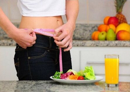 A girl who is losing weight while dieting measures her waist circumference